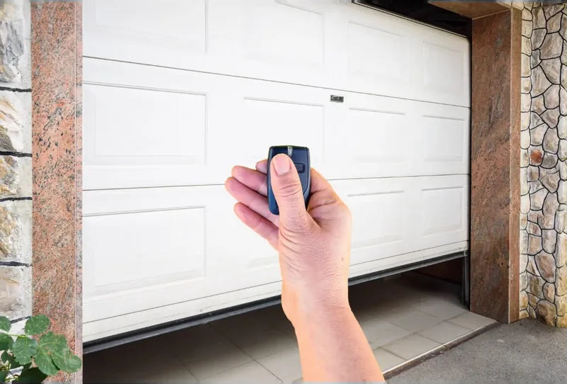 Hand holding a garage door remote in front of a white sectional garage door opening